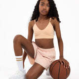 Girl wearing a beige crop top and shorts holding a basketball on a white background.