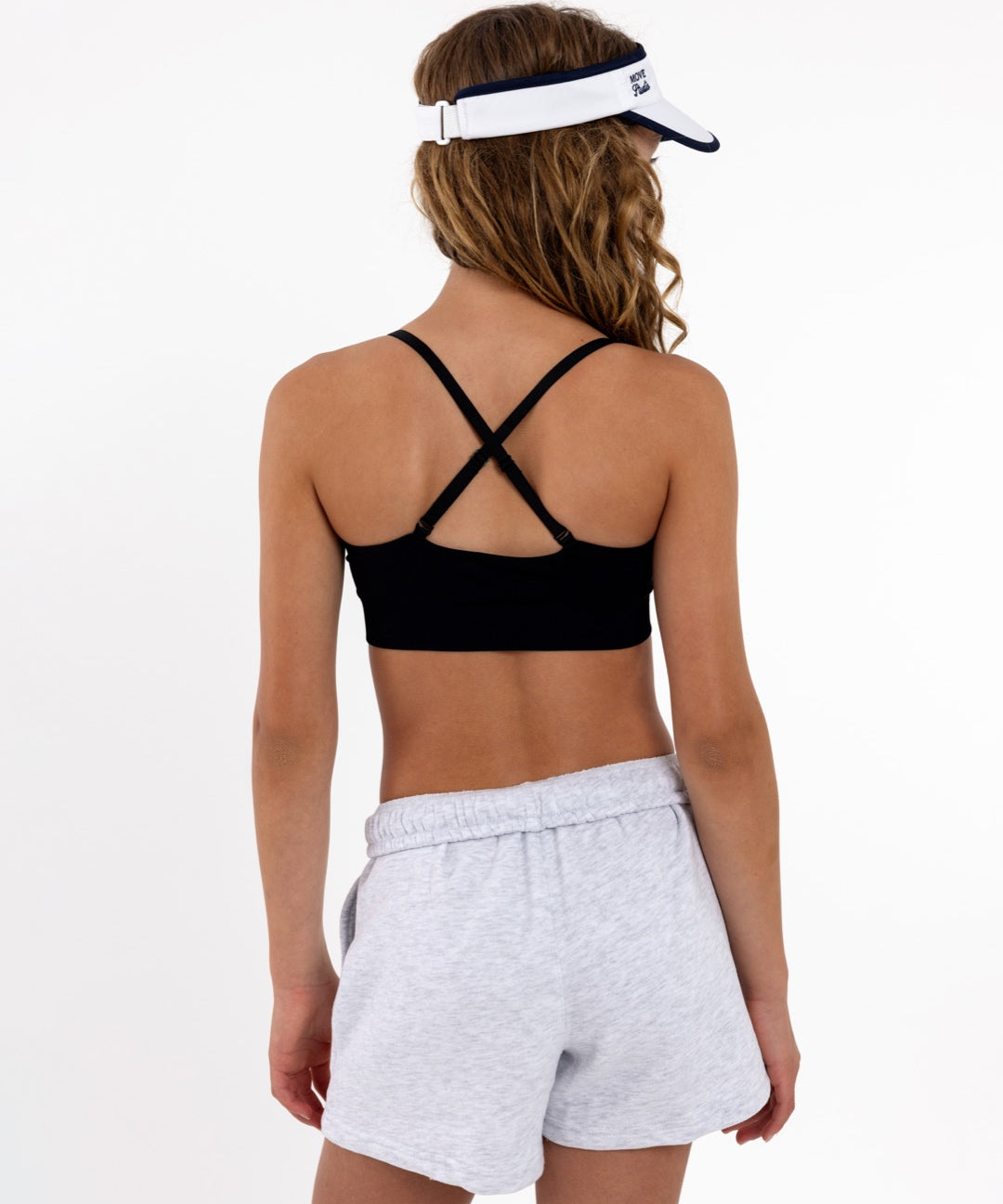 Back view of a girl wearing a black sports  bra showing adjustable criss-cross straps and a seamless crop top fit.