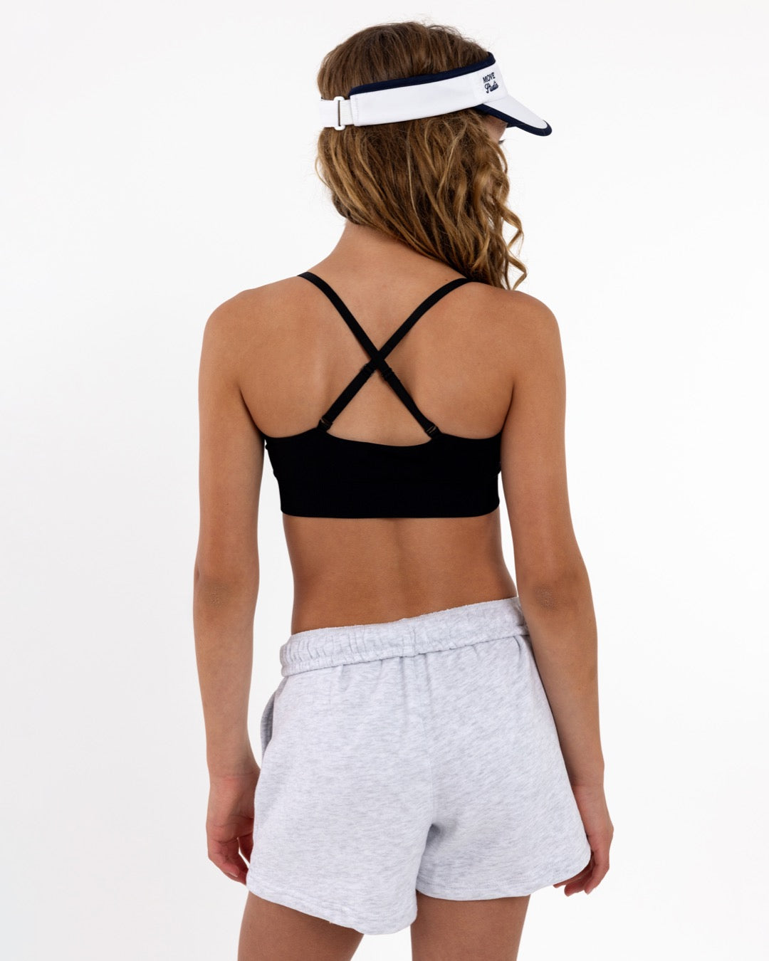 Back view of a girl wearing a black sports  bra showing adjustable criss-cross straps and a seamless crop top fit.