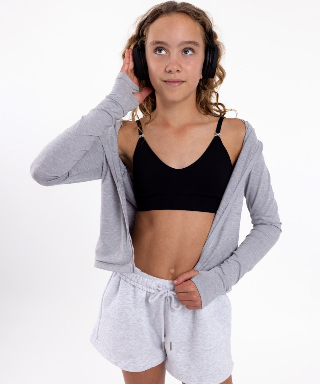 Girl listening to music wearing a black first training bra with a seamless underband and adjustable straps with bow detail.