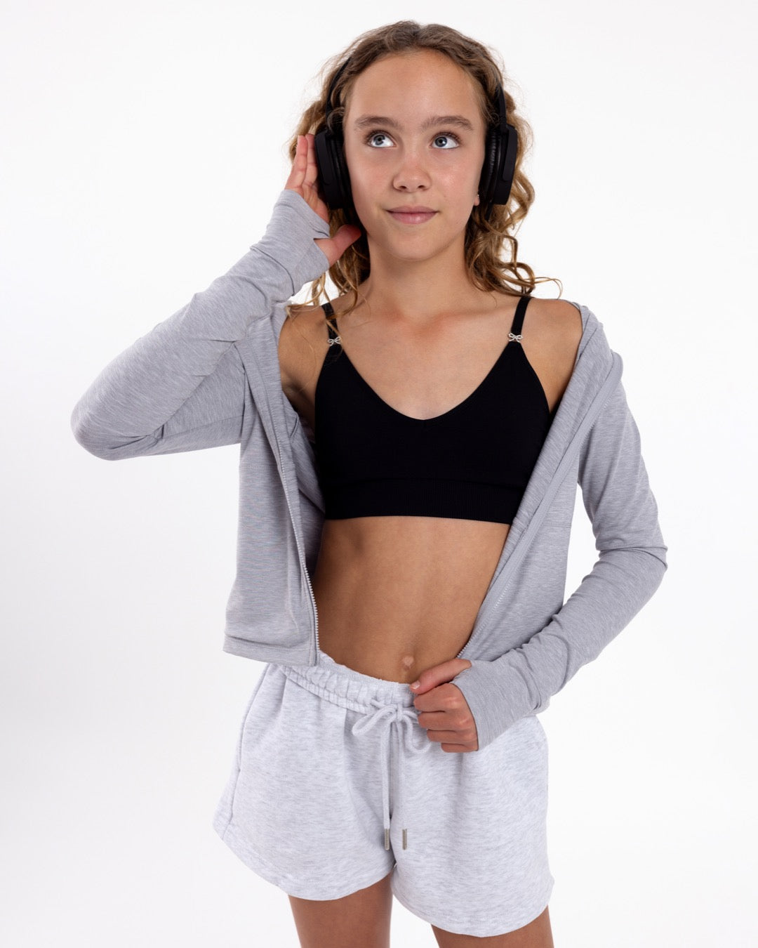 Girl listening to music wearing a black first training bra with a seamless underband and adjustable straps with bow detail.