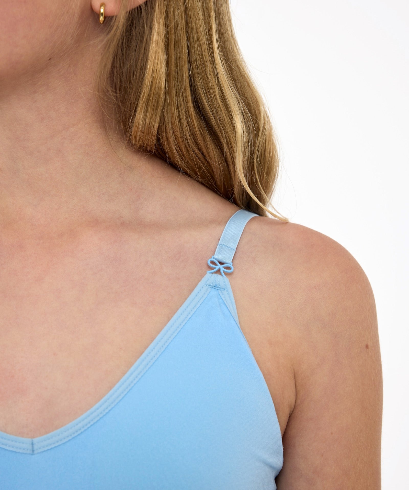 Close-up of a girl wearing a light-blue first training bra showing adjustable straps with bow detail and seamless underband.