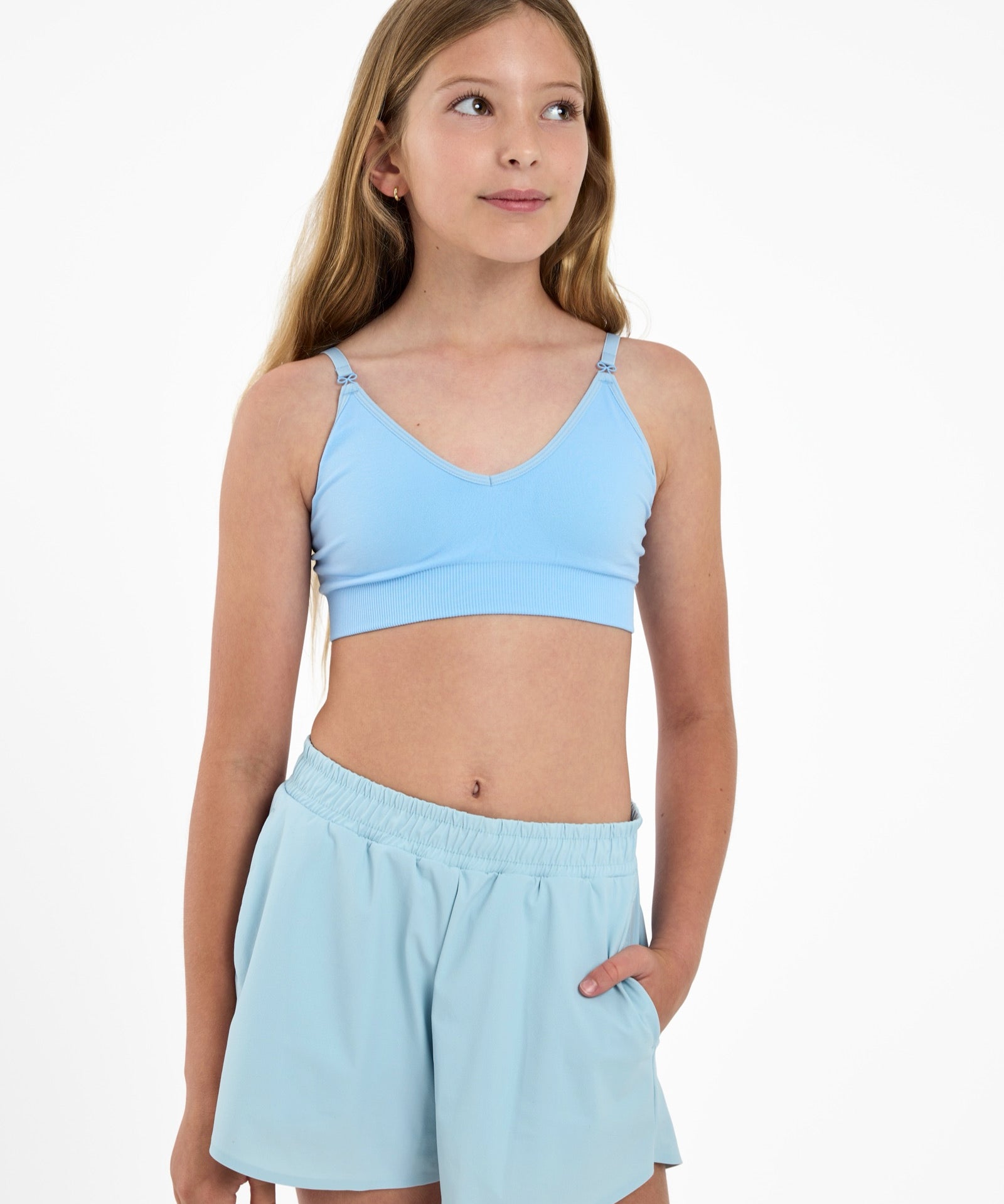 Girl looking up wearing a light-blue first training bra with a seamless underband and adjustable straps with bow detail.