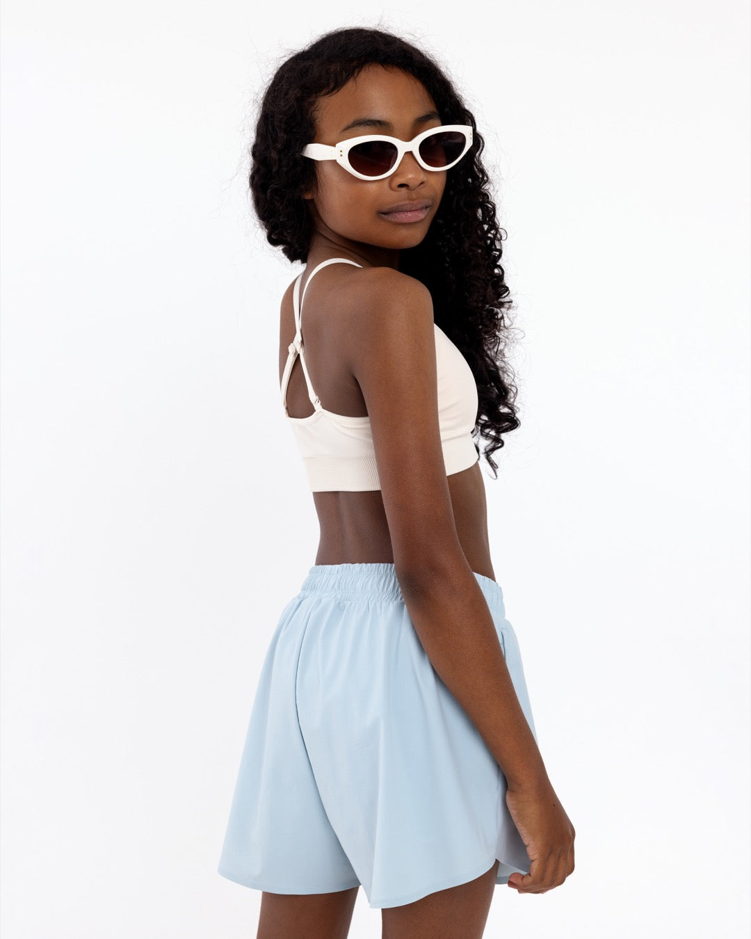 Side view of a girl wearing a white first training bra showing adjustable straps and a seamless crop top fit.