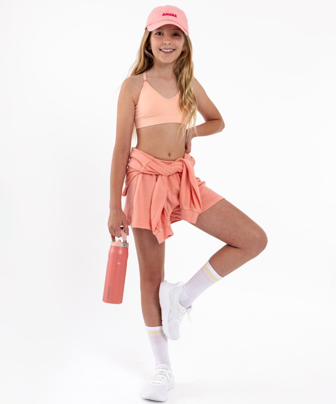 Teen girl wearing a peach crop top sports bra with a seamless underband and adjustable straps.