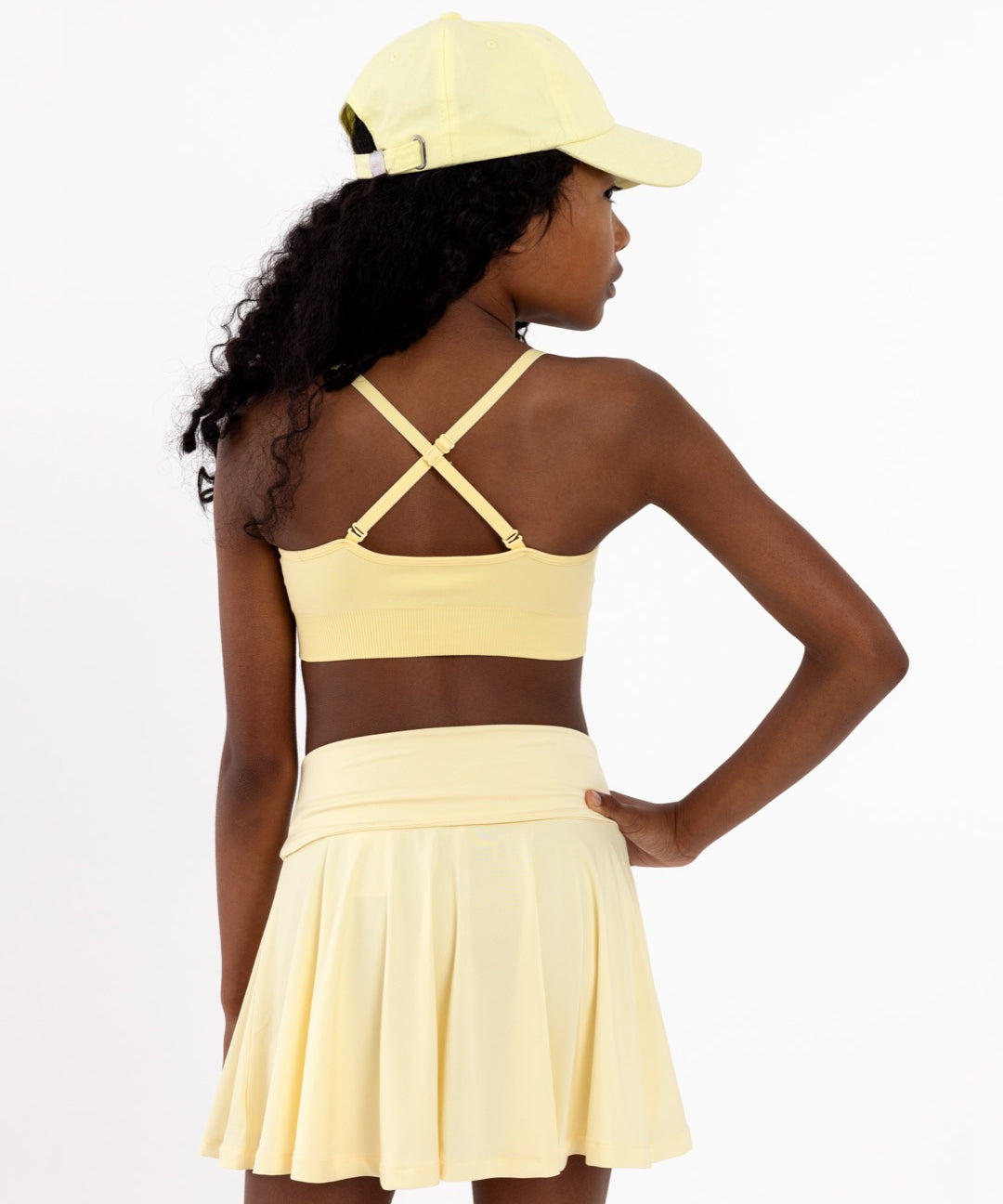 Back view of a girl wearing a yellow first training bra showing adjustable criss-cross straps and a seamless crop top fit.